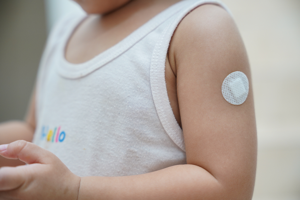 child's arm with a circle bandaid on it indicating that the child has received a vaccination